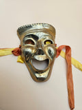 Solid brass comedy theater mask with attached decorative ribbons.