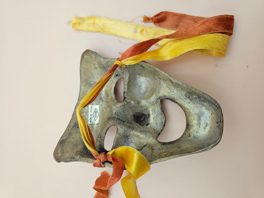 Solid brass comedy theater mask with attached decorative ribbons.